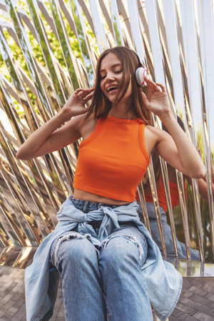 Young beautiful girl listens to music on headphones sitting on a park bench.の写真素材