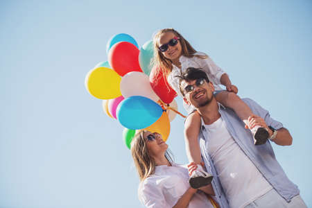 Young smiling family with colorful balloons walking on sunny day. Front view.の写真素材