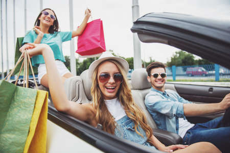 Happy girls returning from store with shopping bags with theirs boyfriend by cabriolet.の写真素材