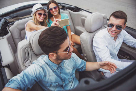 Group of happy friends sitting in the cabriolet. Beautiful girls taking a selfi on rear seats.の写真素材