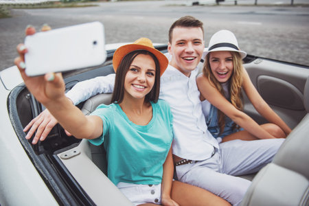 Three beautiful friends taking selfie while sitting in the cabriolet on rear seats.
