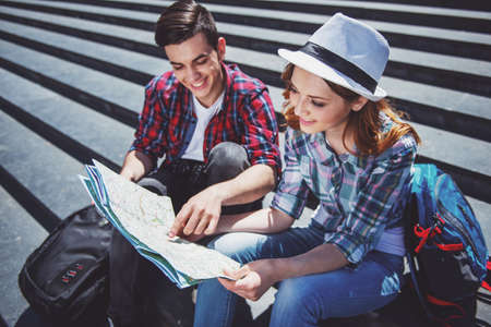 Happy young tourist couple sitting on the stairs together and examining map.の写真素材