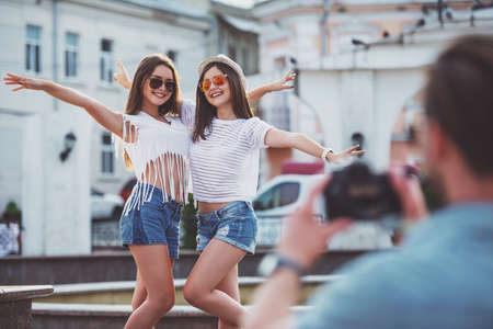 Friendship, leisure and people concept. Rear view of young man is taking photo to his girlfriends with photocamera, outdoors, in the town.の写真素材