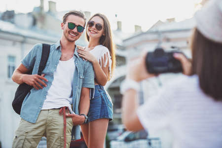 Friendship, leisure and people concept. Rear view of young woman is taking photo to her friends with photocamera, outdoors, in the town.の写真素材