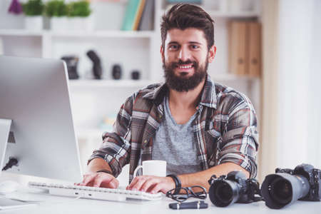 Young cheerful photographer with beard, while working in his officeの写真素材