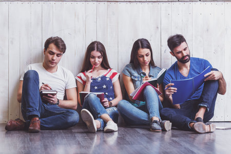 Four attractive young friends sitting on the floor, writing in a notebook