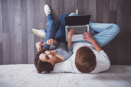 Young couple sitting on Wooden floor, using a laptop at home