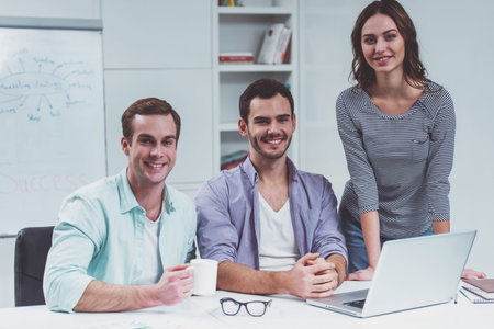 Two young attractive businessmen and one beautiful businesswoman in casual clothes using laptop,...