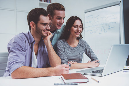 Two young attractive businessmen and one beautiful businesswoman in casual clothes using laptop and...