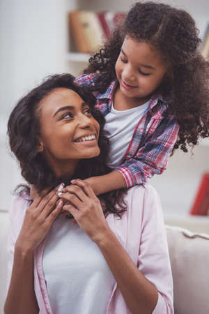 Cute little Afro-American girl hugging her beautiful young mother. Both looking at each other and smiling.の写真素材