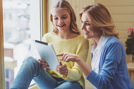 Lovely teenage girl and her beautiful mother using a tablet and smilingの写真素材