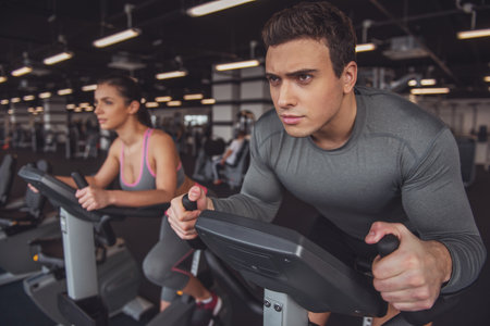 Attractive young muscular people working out on an exercise bike in gymの写真素材