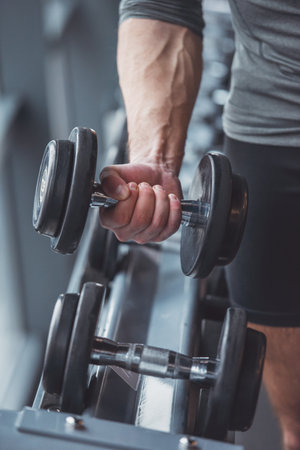 Handsome young muscled man working out with dumbbells in gym, close-upの写真素材