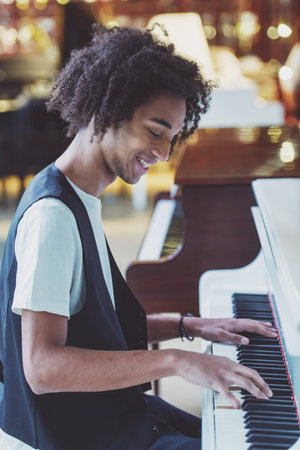 Side view of handsome Afro-American man in classical vest smiling and playing a piano in a musical...