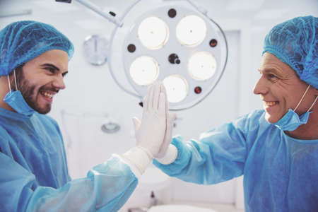 Two handsome doctors are giving high five and smiling, standing in a modern operating roomの写真素材