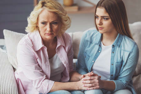 Young daughter is calming her mother while sitting on sofa at homeの写真素材