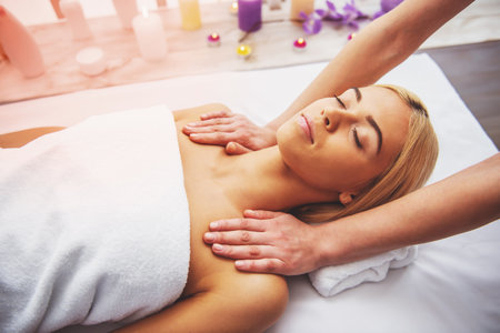 Beautiful blonde girl is lying with closed eyes at spa while a massage therapist is massaging her headの写真素材