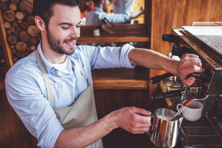 Handsome young barista is making coffee using a modern coffee machine in the urban cafe and smilingの写真素材