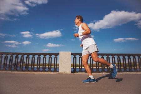 Side view of handsome middle aged man in sports uniform running on the bridgeの写真素材