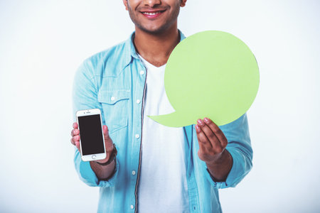 Cropped image of handsome young Afro American smiling, holding speech bubble and smartphone, isolated on white backgroundの写真素材