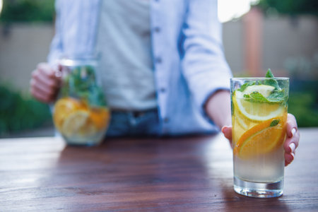Cropped image of young girl is holding a glass of lemonade while standing outdoors. Glass in focusの写真素材