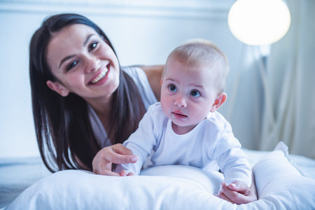 Portrait of beautiful young mom and her sweet little baby looking at camera and smiling, lying on...