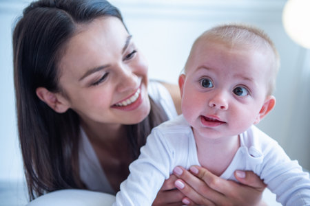 Portrait of beautiful young mom and her sweet little baby smiling, lying on bed at homeの写真素材