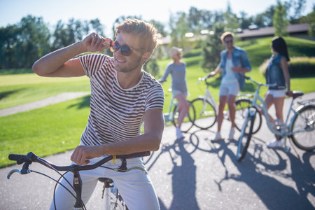 Handsome stylish guy is looking away and smiling while cycling with his friends in the park