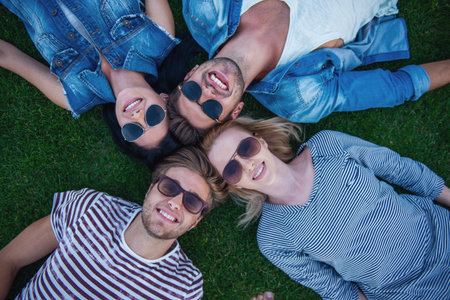 Top view of beautiful stylish friends in sun glasses looking at camera and smiling while lying on...