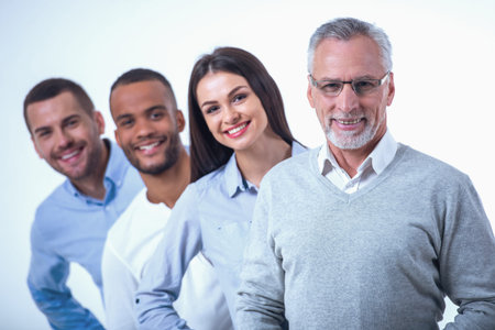 Beautiful business people in smart casual wear are looking at camera and smiling while standing one...