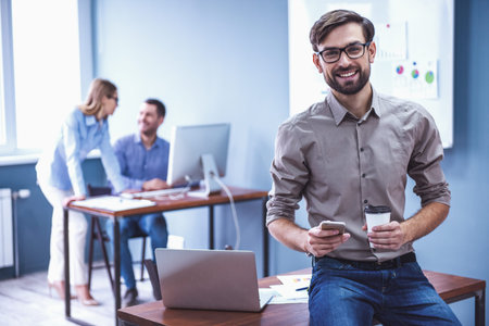 Beautiful business people are working in office. Handsome businessman is holding a cup, looking at...