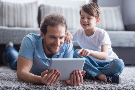 Father and son are using a digital tablet and smiling while spending time together at homeの写真素材