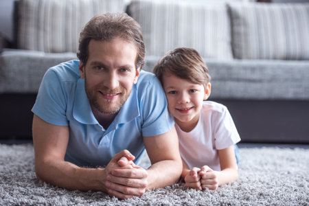 Father and son are looking at camera and smiling while spending time together at homeの写真素材