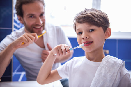 Father and son are looking at camera and smiling while brushing teeth in bathroomの写真素材