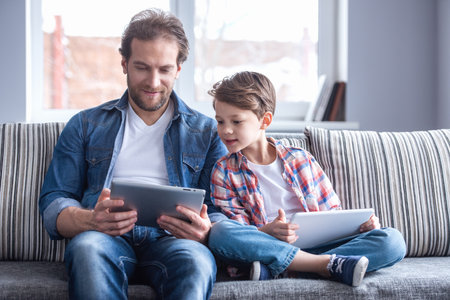 Father and son are using digital tablets and smiling while spending time together at homeの写真素材