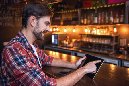 Handsome man is using a digital tablet and smiling while sitting at the bar counter in cafeの写真素材