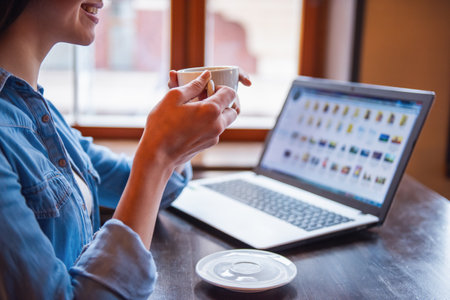 Cropped image of beautiful girl using a laptop, drinking coffee and smiling while sitting at the cafeの写真素材