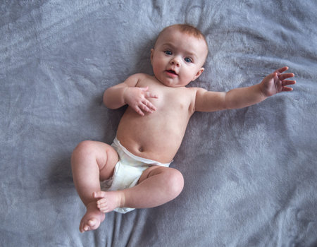 Portrait of cute baby with big blue eyes looking at camera while lying on bed