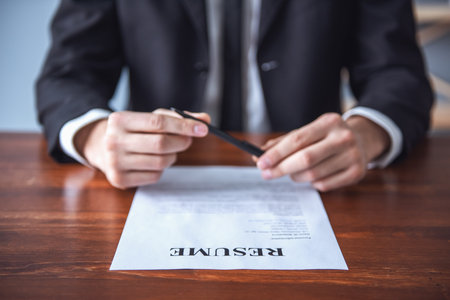 Cropped image of handsome employer examining a resume while sitting at the table in his officeの写真素材