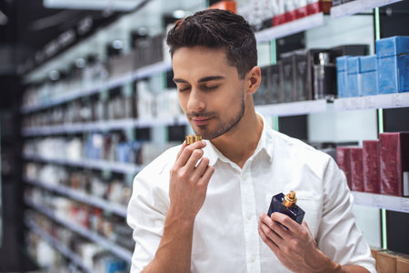Handsome guy is choosing perfumes and smiling while doing shopping in the mallの写真素材