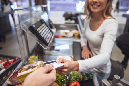 Beautiful young cashier is holding a credit card and smiling while working at the supermarket