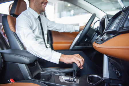 Cropped image of handsome businessman in suit smiling while sitting in a new car in car dealershipの写真素材