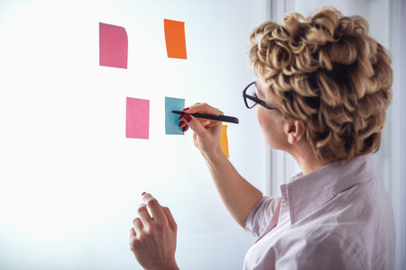 Beautiful psychotherapist in suit and eyeglasses is making notes using stickers and marker