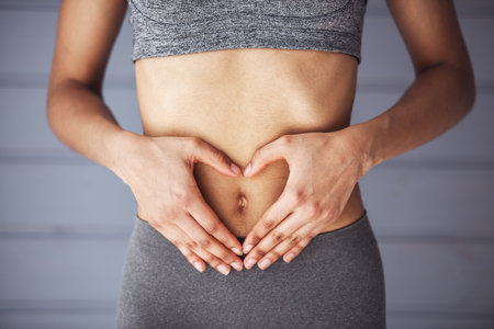 Cropped image of slim girl in sportswear showing heart on her stomachの写真素材