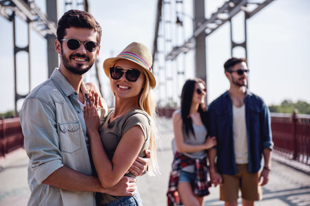 Cheerful young couples are hugging, looking at camera and smiling while walking outdoors
