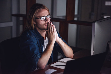 Handsome young businessman with shoulder-length blond hair and in casual wear and eyeglasses is...