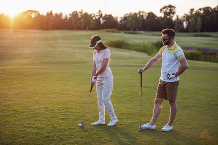 Beautiful young couple is using golf clubs while playing golf togetherの素材 [FY310218242766]