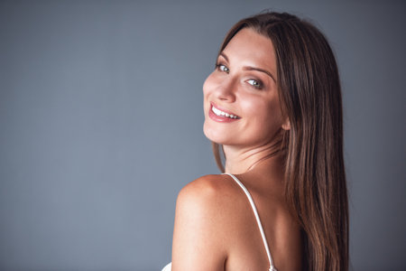 Beautiful woman is looking at camera and smiling, on gray backgroundの写真素材