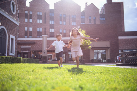 Cheerful kids are holding hands, running and smiling while playing together outdoorsの写真素材
