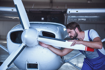 Handsome bearded mechanic in uniform is examining an aircraft in hangarの写真素材